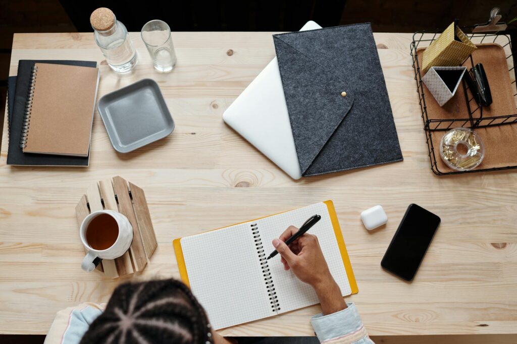 Aerial view of a wooden table workspace with stationery, notebook, and coffee cup.